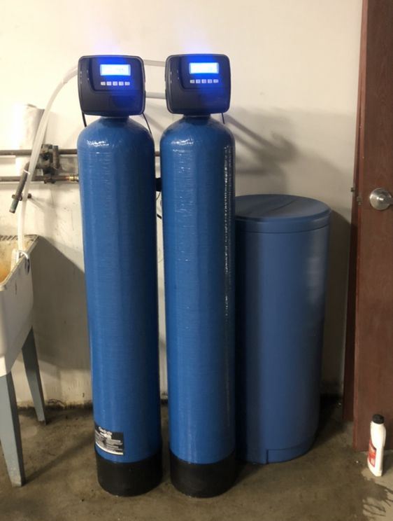 Blue iron filter and water softener tanks, each with a lit digital valve, beside a matching brine tank