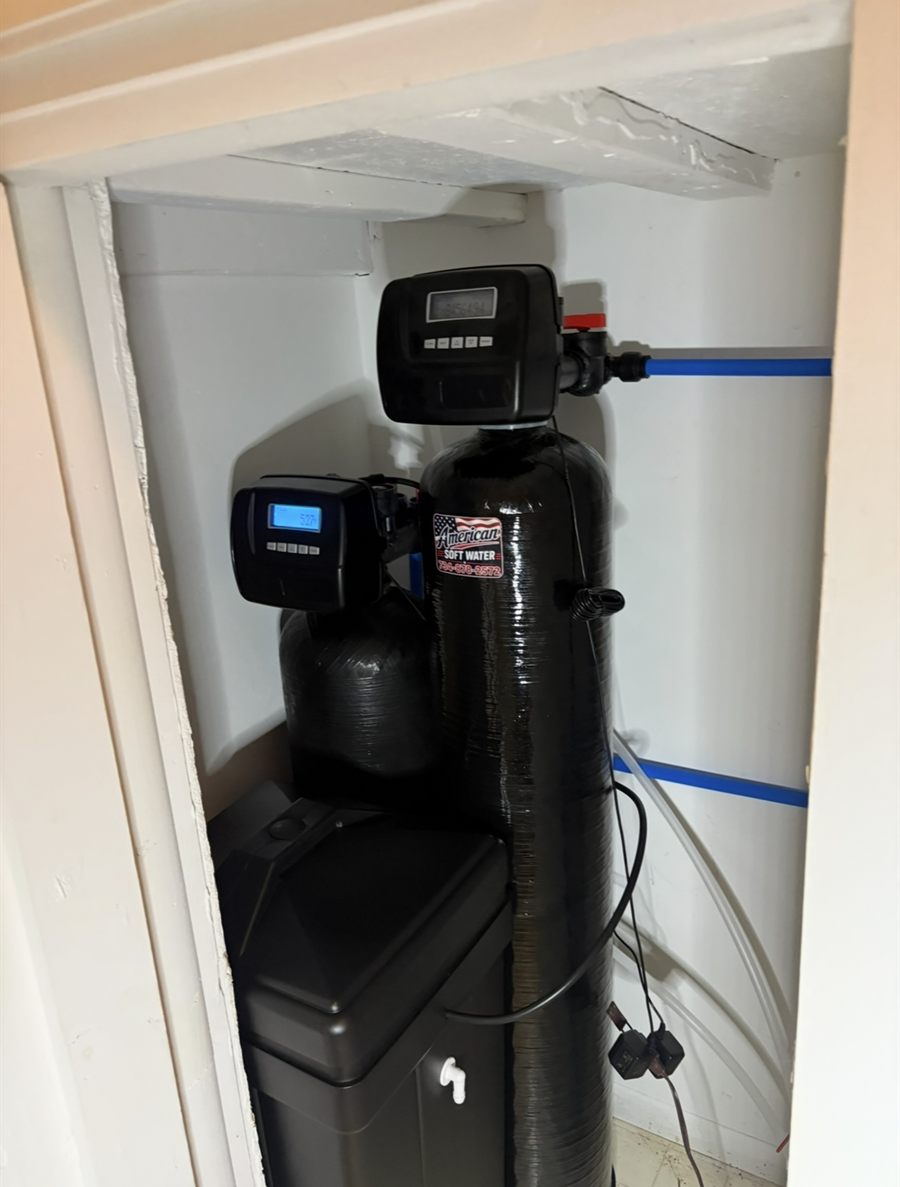 Iron filter and softener fitted into a utility closet, with the American Soft Water sticker on the tank